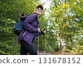 Female tourist with backpack and trekking poles hiking in forest 131678152
