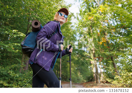 Female tourist with backpack and trekking poles hiking in forest 131678152