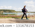 Traveler woman with poles walking along scenic lake shore 131678153