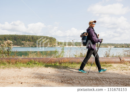 Traveler woman with poles walking along scenic lake shore 131678153