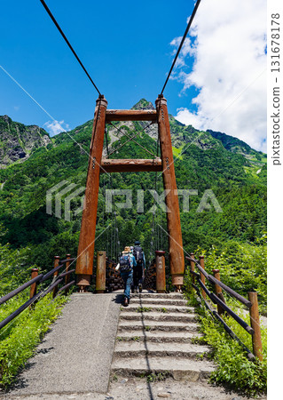Climbers crossing Myojin Bridge in Kamikochi and Mt. Myojin - A refreshing summer mountain scenery Climbers crossing Myojin Bridge in Kamikochi and Mt. Myojin - A refreshing summer mountain scenery 131678178