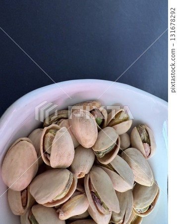 Pistachios in a white bowl. Bowl of pistachios on dark background. Pistachios in a white bowl. Bowl of pistachios on dark background. 131678292