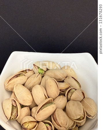 Pistachios in a white bowl. Bowl of pistachios on dark background. Pistachios in a white bowl. Bowl of pistachios on dark background. 131678293