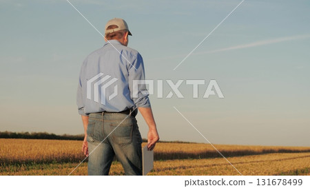 Farmer standing in golden wheat fields with a tablet, Agricultural innovation through technology, Monitoring crop health using a digital tablet, Digital solutions for wheat farming, Farmer integrates 131678499