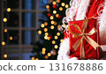 Santa Claus holding a gift while in front of Christmas tree. Christmas spirit, holidays and celebrations concept. 131678886