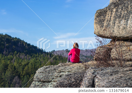 A girl sits on top of a mountain alone. Admires the view on a beautiful sunny day. Travel concept. Background with space for text. 131679014