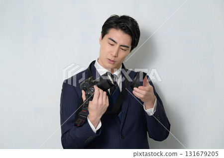 A man in a suit holding a camera and worrying 131679205