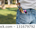 A close-up of paintbrushes and paint tubes in the back pocket of denim jeans. Creative concept symbolizing art, creativity, and inspiration outdoors. 131679792
