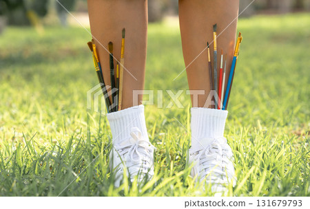 Paintbrushes tucked into white socks and sneakers on green grass. A playful and creative concept combining art, fashion, and outdoor inspiration. Paintbrushes tucked into white socks and sneakers on green grass. A playful and creative concept combining art, fashion, and outdoor inspiration. 131679793