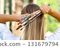 Rear view of a woman gathering colorful, paint-splattered brushes behind her head, long blonde hair and soft bokeh, artistic lifestyle and creativity concept 131679794