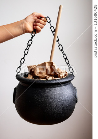 Hand holding black cauldron with wooden stirring stick and brown paper bags Hand holding black cauldron with wooden stirring stick and brown paper bags 131680429
