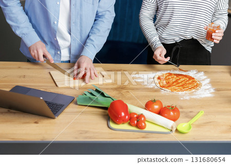 Close up romantic couple is cooking on kitchen. Young man and attractive young woman are having fun together while making salad and pizza. Healthy lifestyle concept. 131680654
