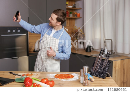 Handsome man cooking in the kitchen and making photo preparing food on his mobile phone. Handsome man cooking in the kitchen and making photo preparing food on his mobile phone. 131680661