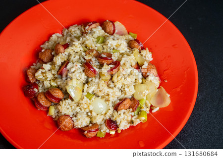 Delicious fried rice with sliced sausages and vegetables on a vibrant red plate. 131680684