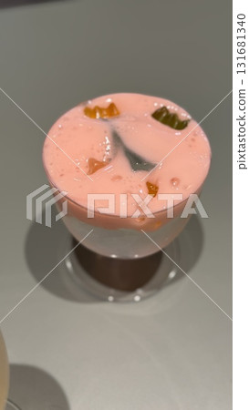 Glass of layered pink and white yogurt dessert with fruit pieces on smooth background 131681340
