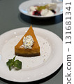 Slice of pumpkin pie with whipped cream and mint garnish on white plate, blurred dessert background 131681341