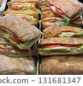 Ciabatta sandwiches with lettuce, tomato, and meat stacked in display case for customers 131681347