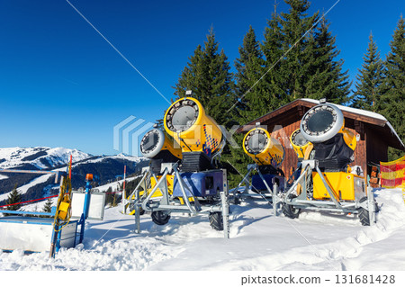 Operating artificial snow cannon near piste making snowy powder.Ski lift ropeway on hilghland alpine mountain winter resort on bright sunny day. downhill slopes with people enjoy sport activities Operating artificial snow cannon near piste making snowy powder.Ski lift ropeway on hilghland alpine mountain winter resort on bright sunny day. downhill slopes with people enjoy sport activities 131681428