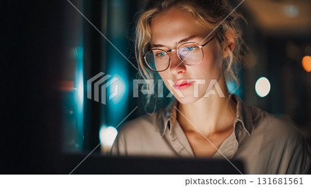 Focused businesswoman working late at night in office. A woman with glasses is illuminated by the glow of a computer screen, working in a dimly lit office. This is AI-generated item 131681561
