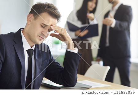 Stressed businessman in office suffering conflict as colleagues argue in background Stressed businessman in office suffering conflict as colleagues argue in background 131682059