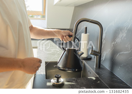 Man filling black kettle with water in modern kitchen sink 131682435