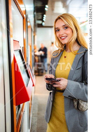 Smiling woman using phone near transportation ticket machine 131682473