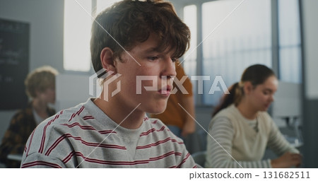 Brown Eyed Boy in Striped Sweater Working on Computer, Looking Closely at Camera Brown Eyed Boy in Striped Sweater Working on Computer, Looking Closely at Camera 131682511