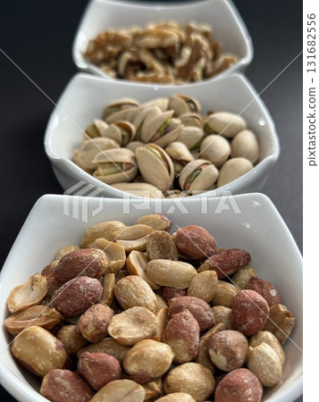 Bowls of pistachios, walnuts, and peanuts on dark background. Assorted nuts in bowls. Bowls of pistachios, walnuts, and peanuts on dark background. Assorted nuts in bowls. 131682556