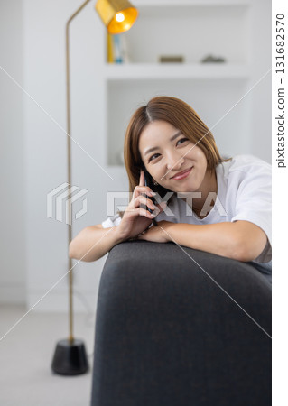 一位年輕女子坐在沙發上，用智慧型手機聊天 131682570