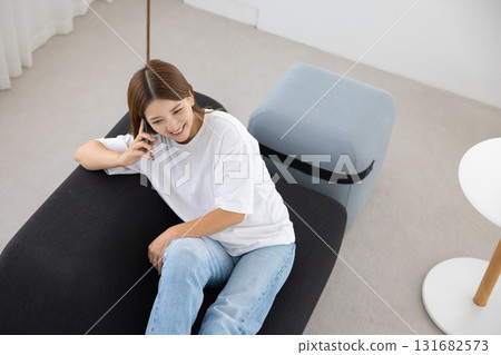 A young woman sitting on a sofa and talking on a smartphone 131682573