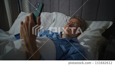 Mature Gray Haired Man In Glasses Lying In Bed With Smartphone In Hand Mature Gray Haired Man In Glasses Lying In Bed With Smartphone In Hand 131682612