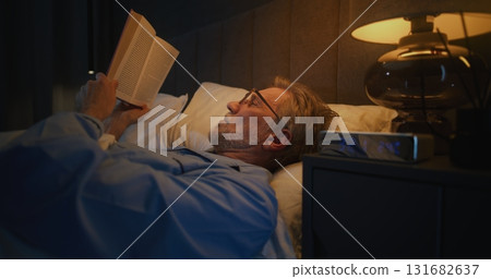 Mature Man Wearing Glasses Reads in Bed Few Hours Before Dawn Mature Man Wearing Glasses Reads in Bed Few Hours Before Dawn 131682637