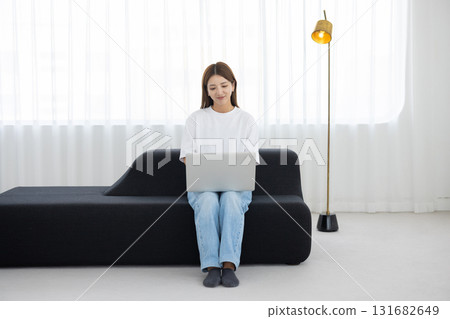 Young woman sitting on sofa and working on computer Young woman sitting on sofa and working on computer 131682649