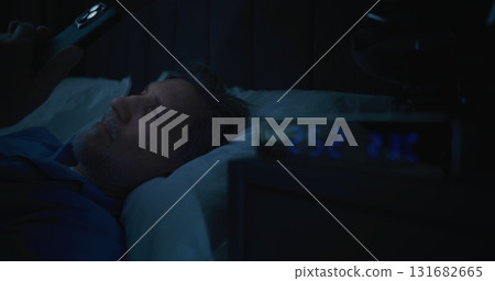 Mature Man in Bed Illuminated By Smartphone Screen, Digital Clock Showing Two AM 131682665