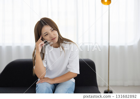A young woman sitting on a sofa and looking troubled 131682892
