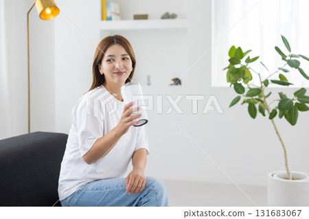 A young woman sitting on a sofa with a tumbler in her hand 131683067