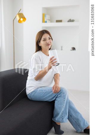 A young woman sitting on a sofa with a tumbler in her hand A young woman sitting on a sofa with a tumbler in her hand 131683068
