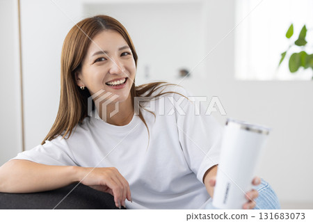 A young woman sitting on a sofa with a tumbler in her hand 131683073