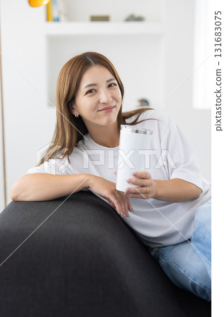 A young woman sitting on a sofa with a tumbler in her hand 131683075