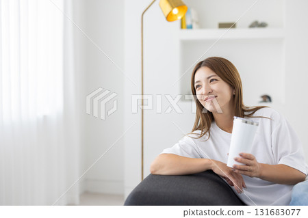 A young woman sitting on a sofa with a tumbler in her hand 131683077