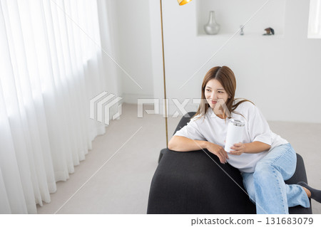 一位年輕女子坐在沙發上，手裡拿著一個玻璃杯 131683079
