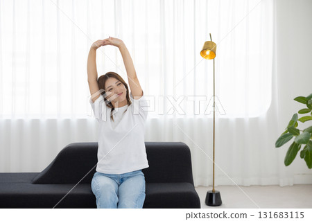 Young woman sitting on sofa and stretching Young woman sitting on sofa and stretching 131683115