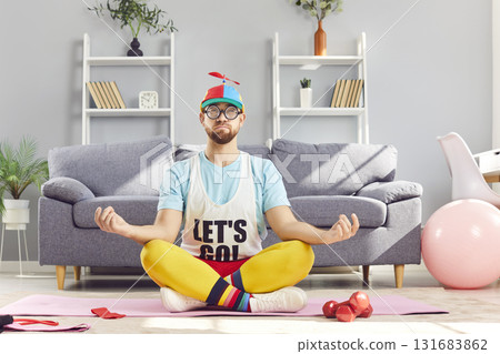 Funny man relaxing sitting on floor on yoga mat in Lotus pose, meditating at home. Funny man relaxing sitting on floor on yoga mat in Lotus pose, meditating at home. 131683862