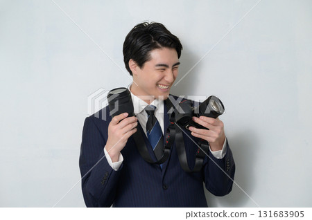 A man in a suit holding a camera and lens and looking happy A man in a suit holding a camera and lens and looking happy 131683905