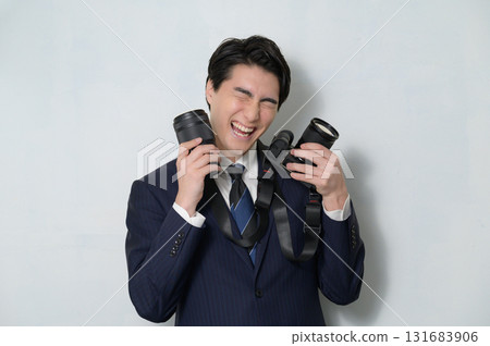 A man in a suit holding a camera and lens and looking happy A man in a suit holding a camera and lens and looking happy 131683906