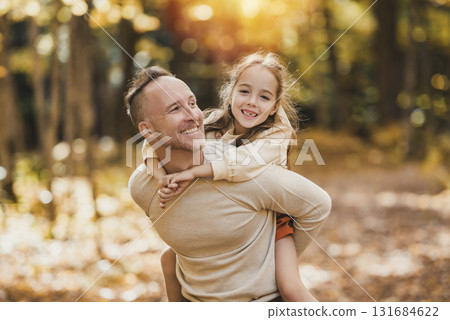Mature father giving piggyback ride to small daughter on a walk in autumn forest. Mature father giving piggyback ride to small daughter on a walk in autumn forest. 131684622