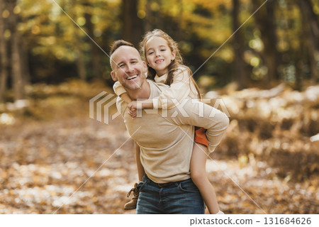 Mature father giving piggyback ride to small daughter on a walk in autumn forest. Mature father giving piggyback ride to small daughter on a walk in autumn forest. 131684626