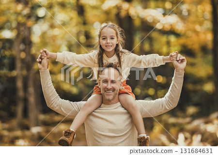 Mature father with daughter on shoulder ride to small daughter on a walk in autumn forest. Mature father with daughter on shoulder ride to small daughter on a walk in autumn forest. 131684631