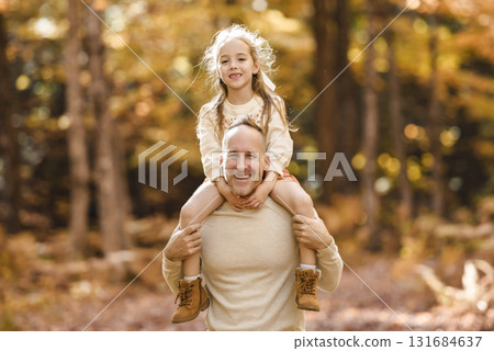 Mature father with daughter on shoulder ride to small daughter on a walk in autumn forest. Mature father with daughter on shoulder ride to small daughter on a walk in autumn forest. 131684637