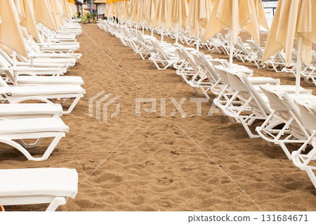 Beach scene with empty closed umbrellas and sun loungers on on sea shore 131684671